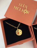 Gold necklace with a pendant in an open jewelry box labeled 'SIÓN MELLOR'.