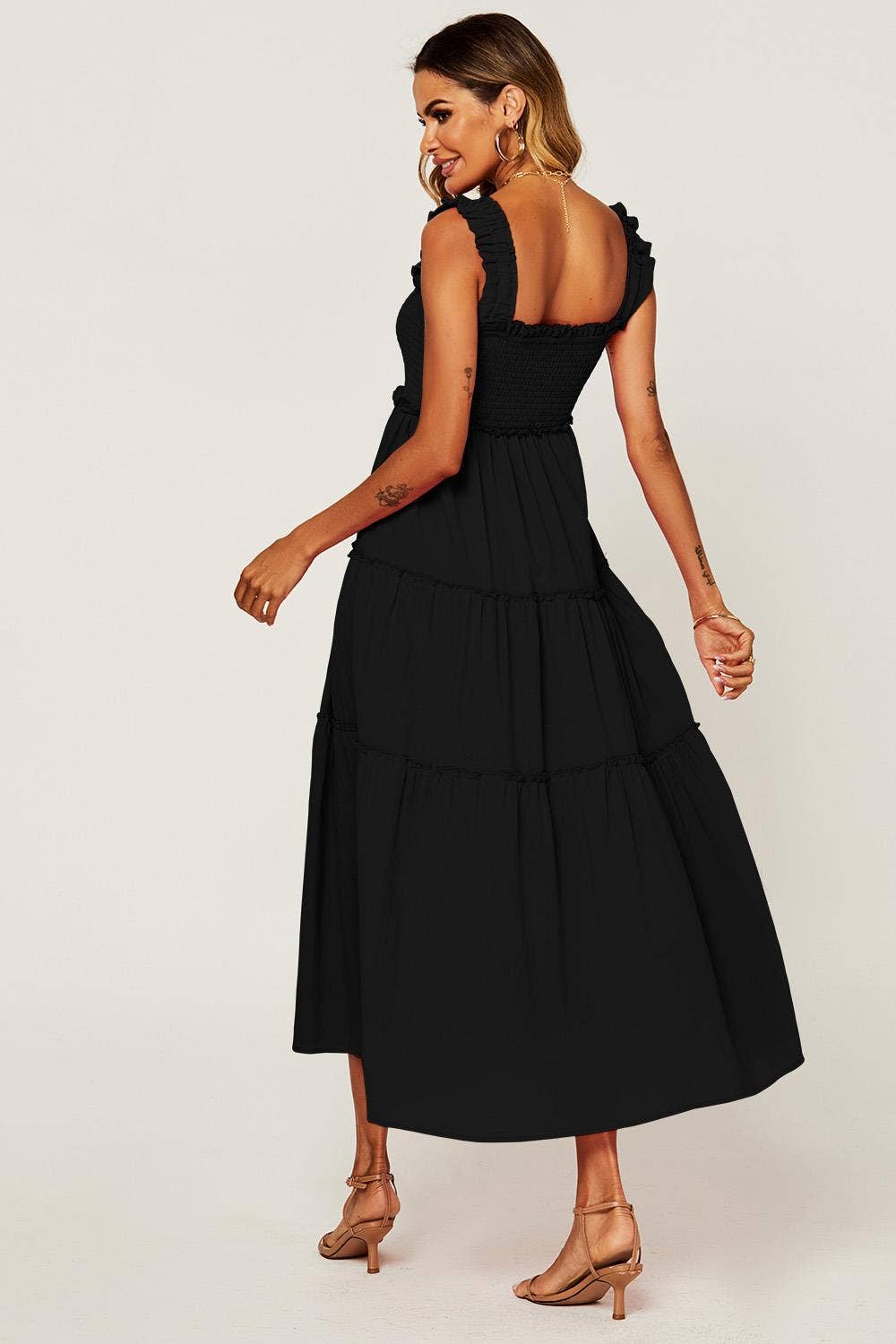 A woman modeling a black sleeveless midi dress with a smocked bodice, ruffled shoulder straps, and a tiered skirt, shown from the back against a plain light background.
